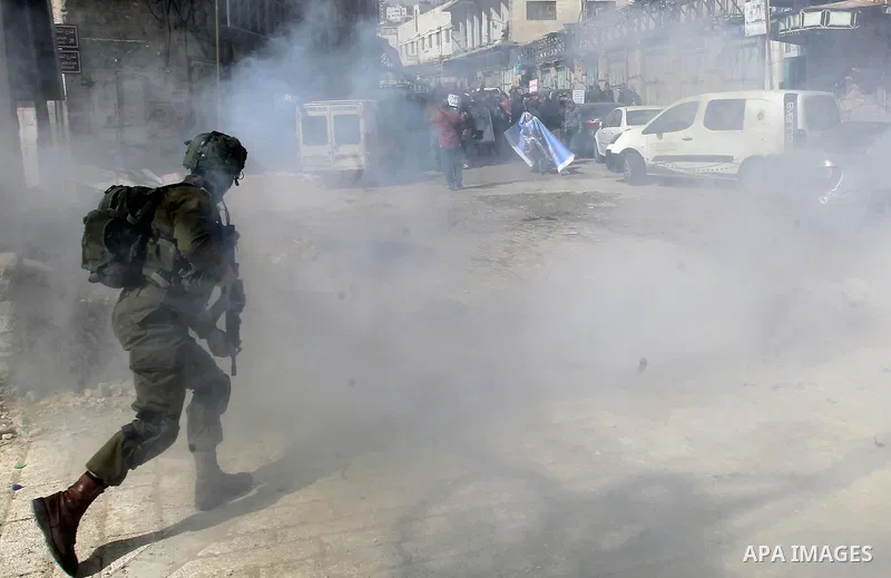 An Israeli soldier runs as tear gas is fired during clashes with Palestinian protesters following a demonstration demanding to dismantle the Ghetto, to mark the 24th anniversary of Ibrahimi mosque massacre when Baruch Go...