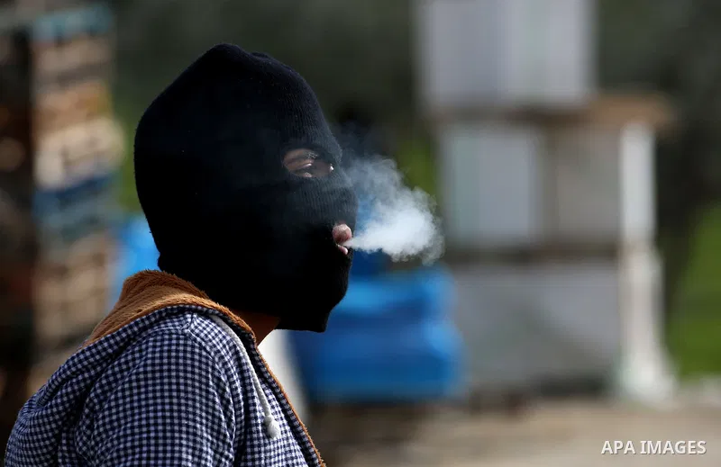 A masked Palestinian protester smokes during clashes with Israeli security forces in the occupied West Bank village of Baita, just outside of Nablus, on February 16, 2018. Photo by Shadi Jarar'ah