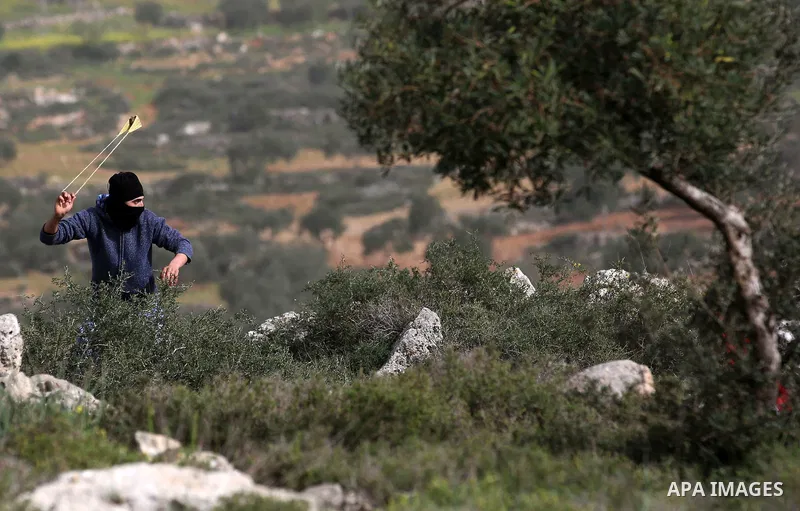 A Palestinian protester uses a slingshot to hurl stones towards Israeli security forces during clashes in the occupied West Bank village of Baita, just outside of Nablus, on February 16, 2018. Photo by Shadi Jarar'ah