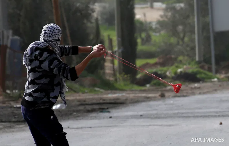 A Palestinian protester uses a slingshot to hurl stones towards Israeli security forces during clashes in the occupied West Bank village of Baita, just outside of Nablus, on February 16, 2018. Photo by Shadi Jarar'ah
