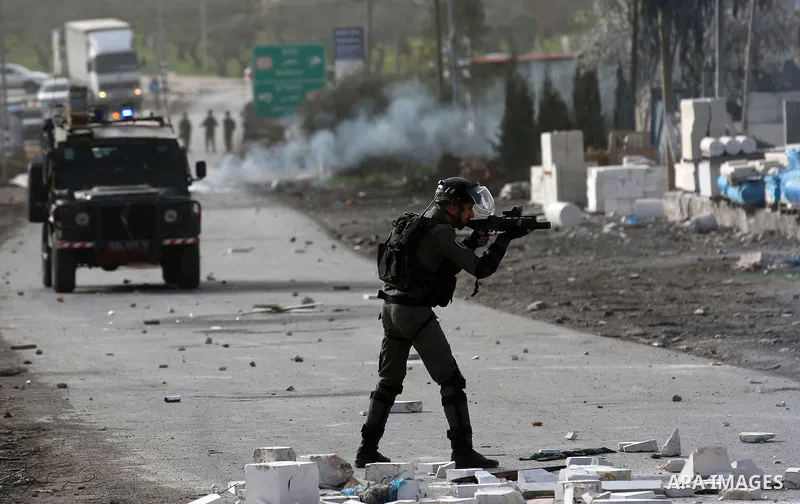 A member of Israeli security forces aims his weapon towards Palestinian protesters during clashes in the occupied West Bank village of Baita, outside of Nablus, on February 16, 2018. Photo by Shadi Jarar'ah