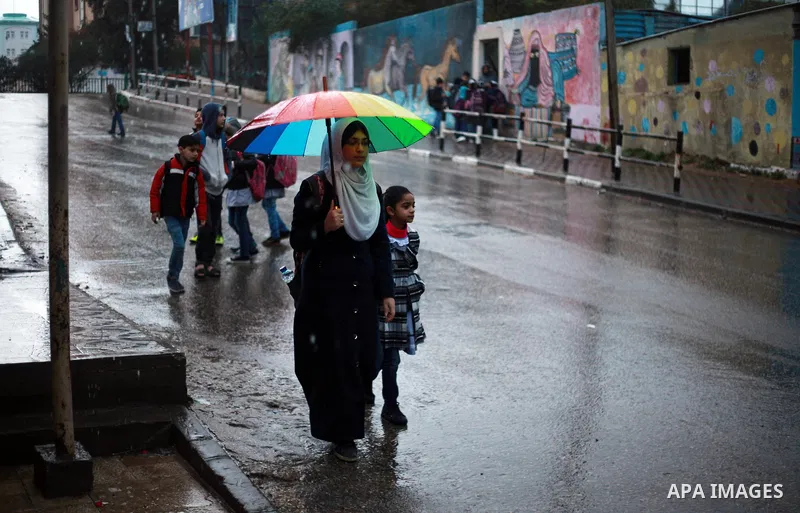 Palestinian school children walk in a flooded street during heavy rain in Gaza City on February 18, 2018. Photo by Mahmoud Ajour
