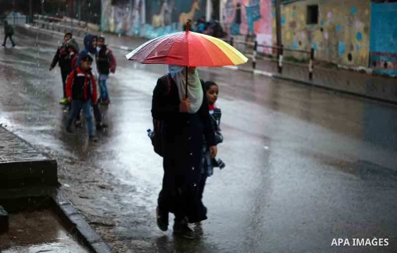 Palestinian school children walk in a flooded street during heavy rain in Gaza City on February 18, 2018. Photo by Mahmoud Ajour