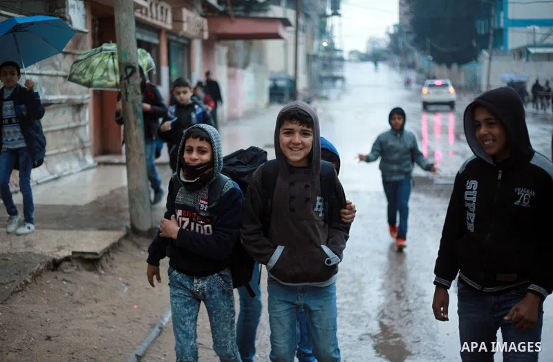 Palestinian school children walk in a flooded street during heavy rain in Gaza City on February 18, 2018. Photo by Mahmoud Ajour