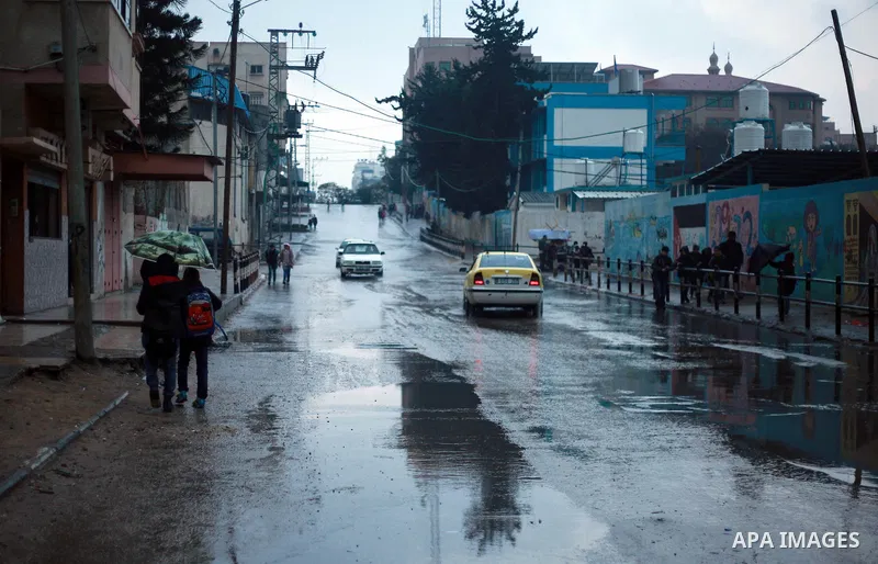 Palestinian school children walk in a flooded street during heavy rain in Gaza City on February 18, 2018. Photo by Mahmoud Ajour