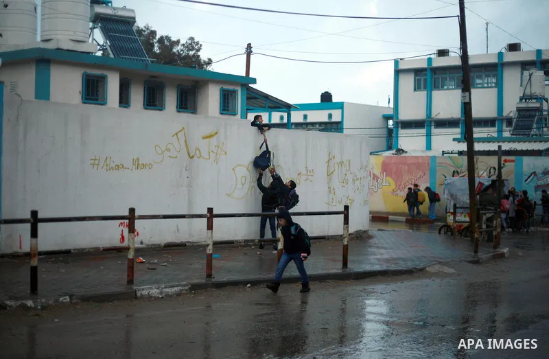 Palestinian school children walk in a flooded street during heavy rain in Gaza City on February 18, 2018. Photo by Mahmoud Ajour