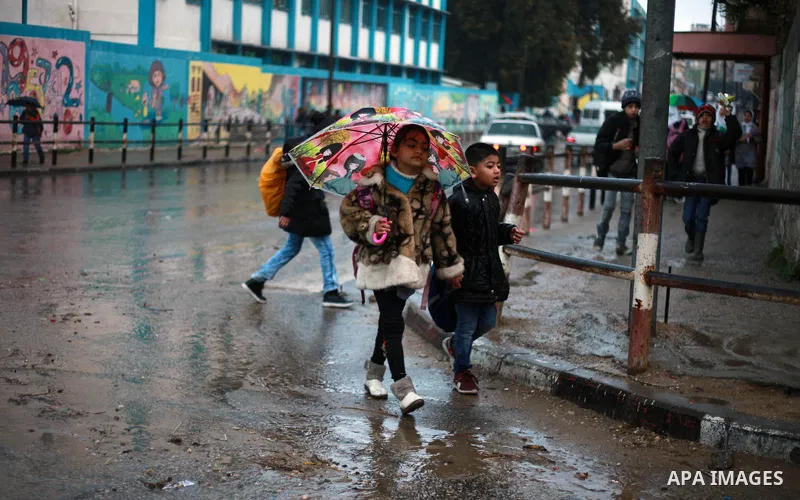 Palestinian school children walk in a flooded street during heavy rain in Gaza City on February 18, 2018. Photo by Mahmoud Ajour