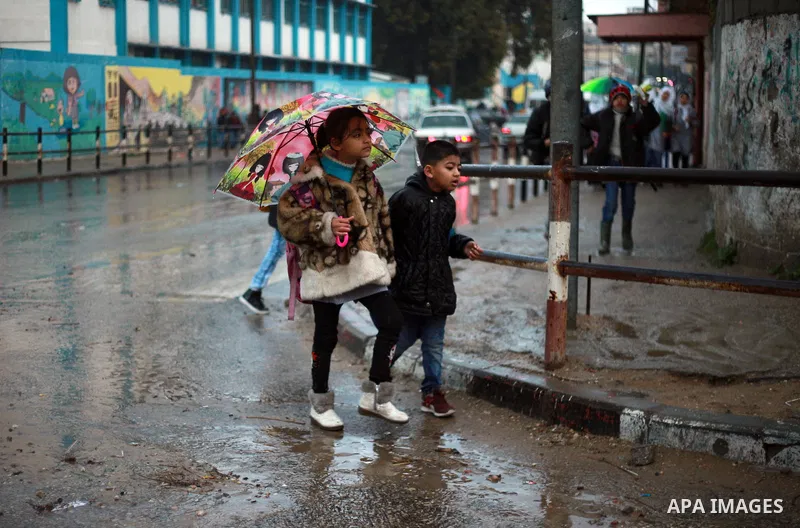 Palestinian school children walk in a flooded street during heavy rain in Gaza City on February 18, 2018. Photo by Mahmoud Ajour