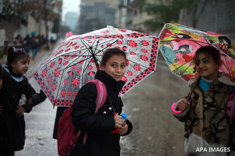 Palestinian school children walk in a flooded street during heavy rain in Gaza City on February 18, 2018. Photo by Mahmoud Ajour