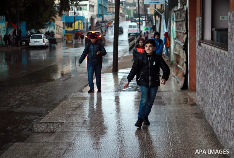 Palestinian school children walk in a flooded street during heavy rain in Gaza City on February 18, 2018. Photo by Mahmoud Ajour