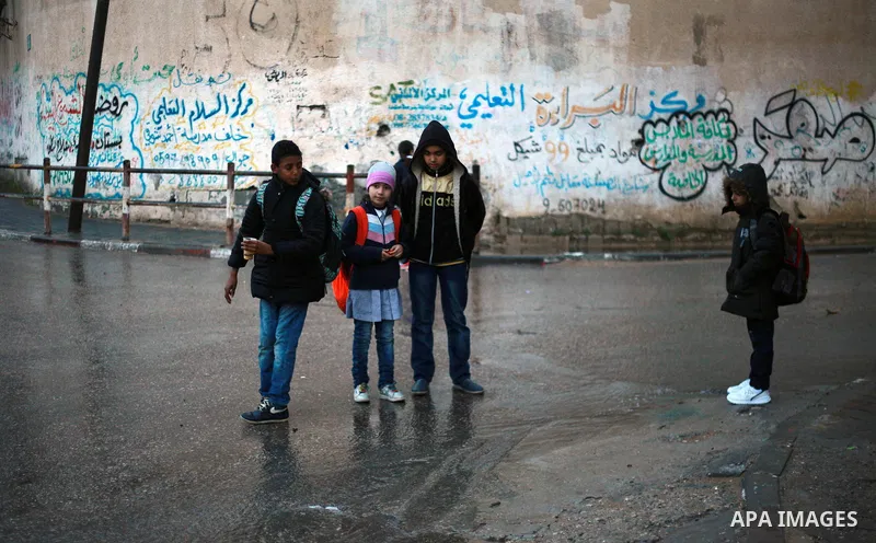 Palestinian school children walk in a flooded street during heavy rain in Gaza City on February 18, 2018. Photo by Mahmoud Ajour