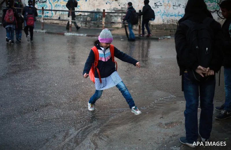 Palestinian school children walk in a flooded street during heavy rain in Gaza City on February 18, 2018. Photo by Mahmoud Ajour