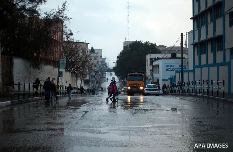 Palestinian school children walk in a flooded street during heavy rain in Gaza City on February 18, 2018. Photo by Mahmoud Ajour