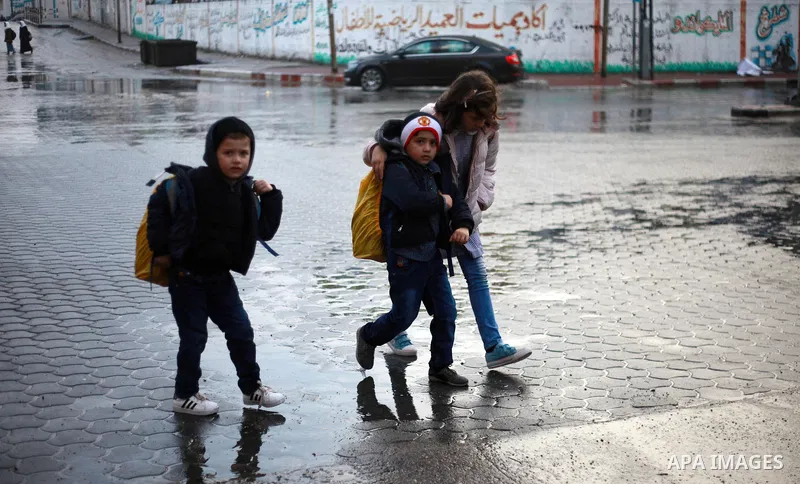 Palestinian school children walk in a flooded street during heavy rain in Gaza City on February 18, 2018. Photo by Mahmoud Ajour
