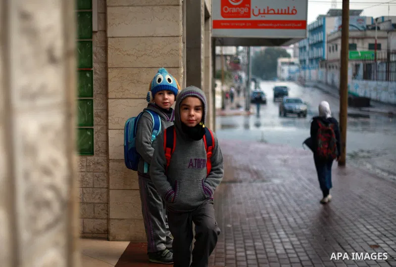 Palestinian school children walk in a flooded street during heavy rain in Gaza City on February 18, 2018. Photo by Mahmoud Ajour