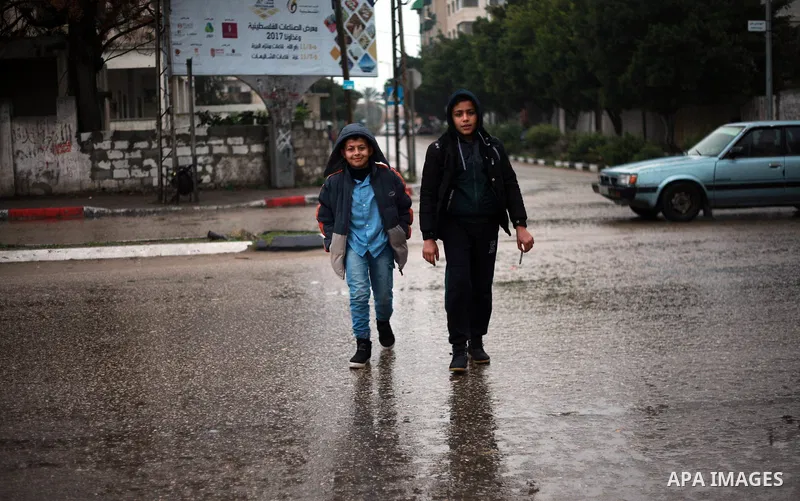 Palestinian school children walk in a flooded street during heavy rain in Gaza City on February 18, 2018. Photo by Mahmoud Ajour