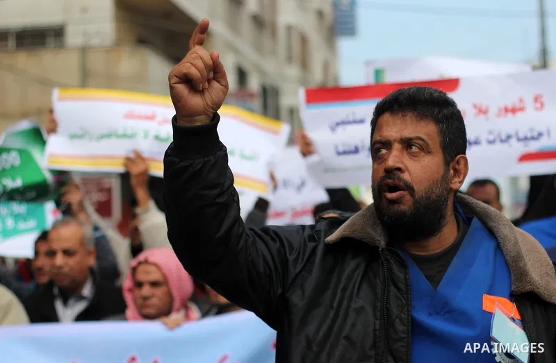 Palestinian cleaners hold banners during a protest to demand their salaries, in Gaza City on February 18, 2018. Photo by Mahmoud Ajour