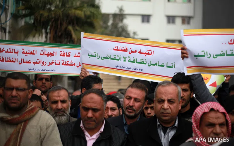 Palestinian cleaners hold banners during a protest to demand their salaries, in Gaza City on February 18, 2018. Photo by Mahmoud Ajour