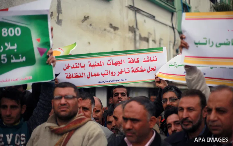 Palestinian cleaners hold banners during a protest to demand their salaries, in Gaza City on February 18, 2018. Photo by Mahmoud Ajour