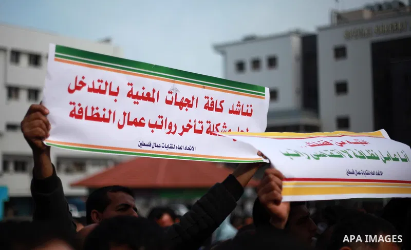 Palestinian cleaners hold banners during a protest to demand their salaries, in Gaza City on February 18, 2018. Photo by Mahmoud Ajour
