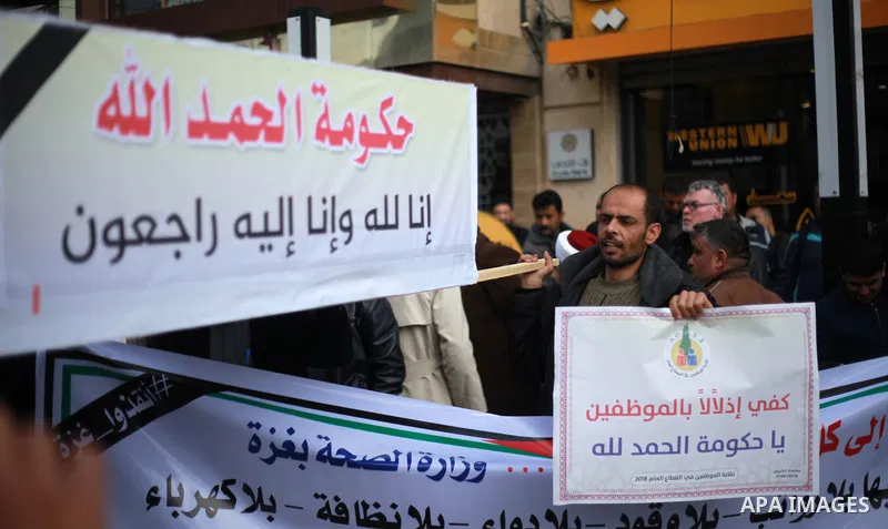 Palestinian employees of Gaza strip hold banners during a demonstration demanding their salaries in Gaza city on February 19, 2018. Photo by Mahmoud Ajour