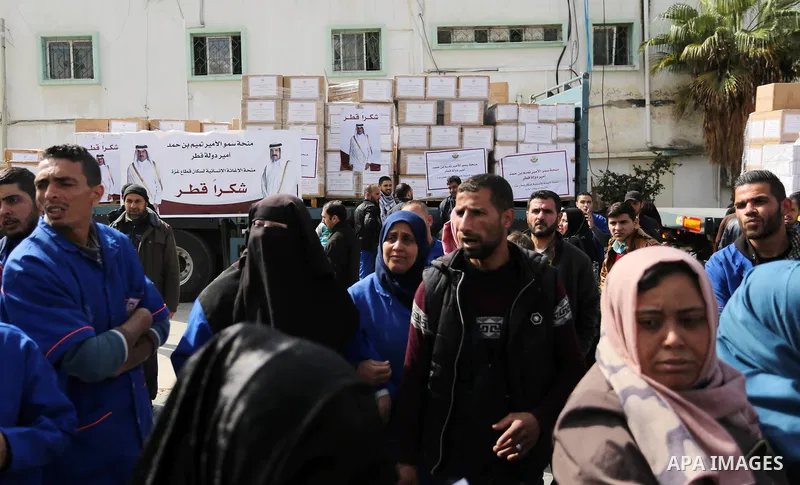 Palestinians walk near the vehicles loaded with humanity aids from Qatar at al-Shifa hospital in Gaza city on February 19, 2018. Photo by Ashraf Amra