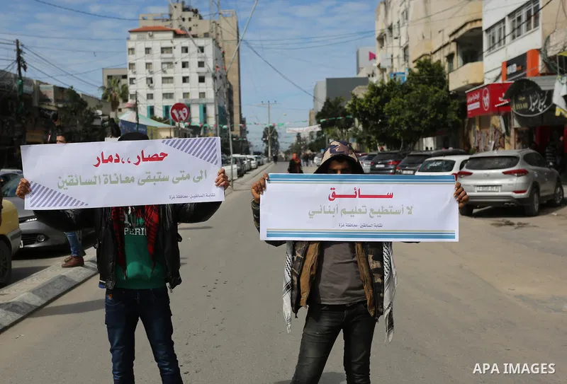 Palestinians hold banners in Gaza City on February 20, 2018 during a general strike to protest the humanitarian situation in Gaza. Photo by Ashraf Amra