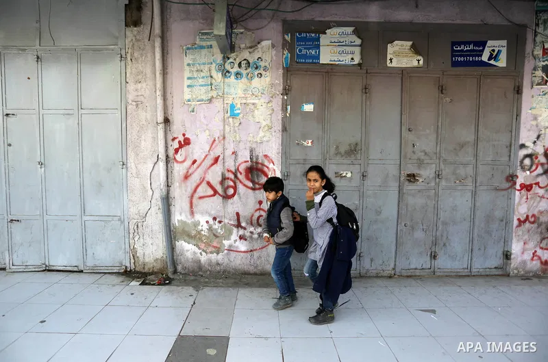 Palestinians walk past closed shops in Gaza City on February 20, 2018 during a general strike to protest the humanitarian situation in Gaza. Photo by Ashraf Amra