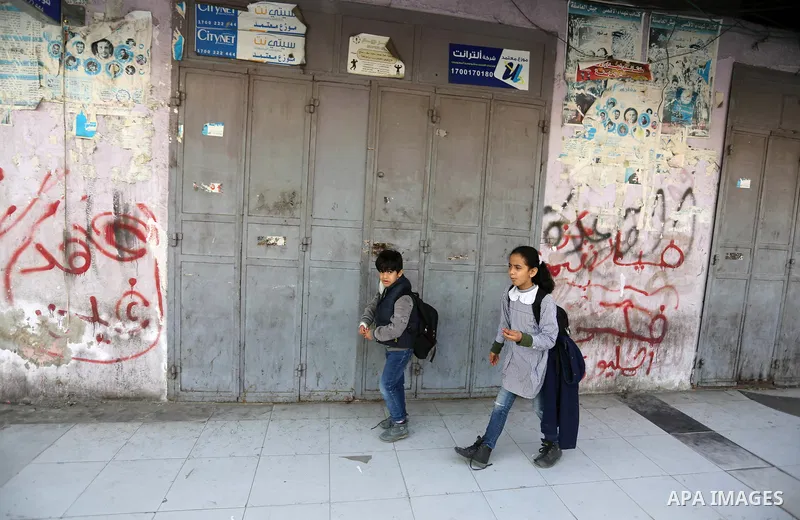 Palestinians walk past closed shops in Gaza City on February 20, 2018 during a general strike to protest the humanitarian situation in Gaza. Photo by Ashraf Amra