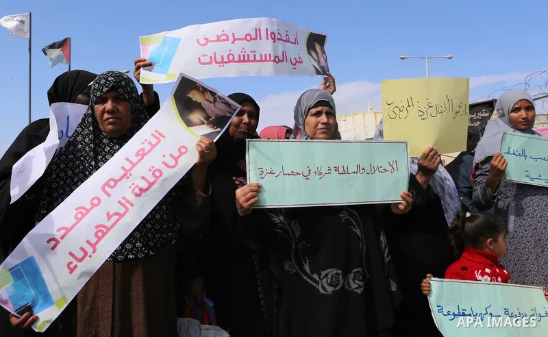 Palestinian women hold banners during a protest calling for an end to the power crisis, outside the power plant in the central Gaza Strip on February 27, 2018. Photo by Yasser Qudih