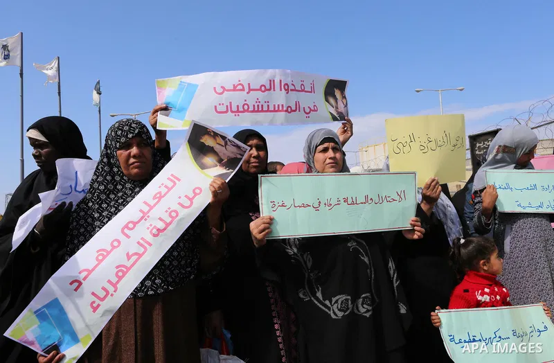 Palestinian women hold banners during a protest calling for an end to the power crisis, outside the power plant in the central Gaza Strip on February 27, 2018. Photo by Yasser Qudih