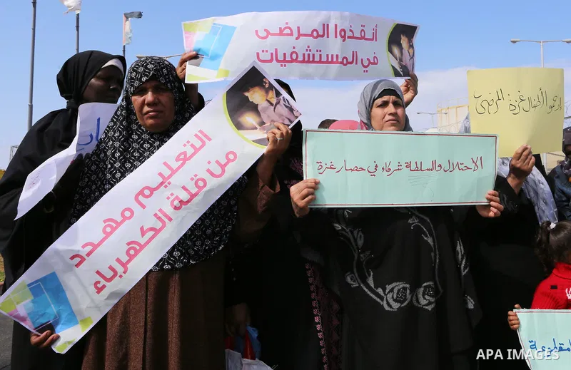 Palestinian women hold banners during a protest calling for an end to the power crisis, outside the power plant in the central Gaza Strip on February 27, 2018. Photo by Yasser Qudih