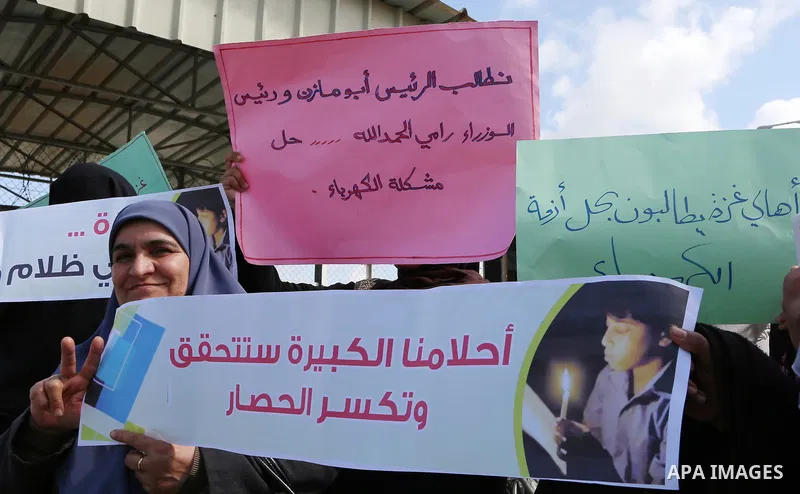 Palestinian women hold banners during a protest calling for an end to the power crisis, outside the power plant in the central Gaza Strip on February 27, 2018. Photo by Yasser Qudih
