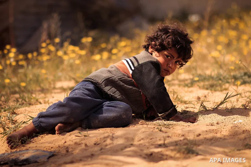 A boy lies on the sand with hard look. Photo by Sanad Ltefa