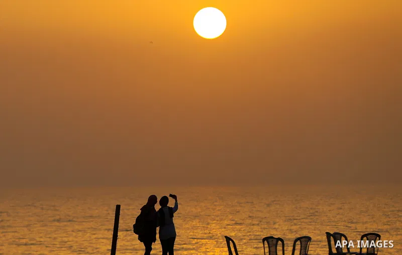 Palestinian girls take a selfie on the beach of Gaza city during sunset on March 5, 2018. Photo by Yasser Qudih