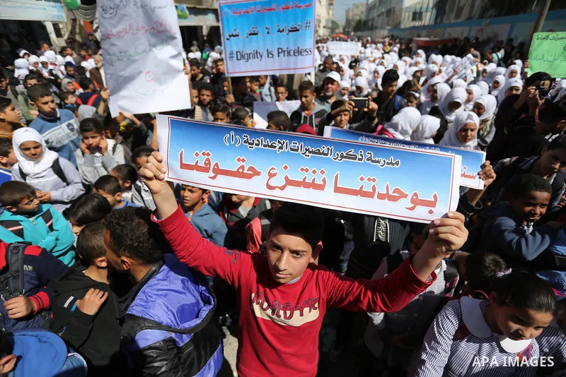 Palestinian school students shout slogans and hold placards in a protest against the US move to freeze funding for the UN agency for Palestinian refugees on March 7, 2018 at the al-Nusairat refugee camp, in central Gaza...