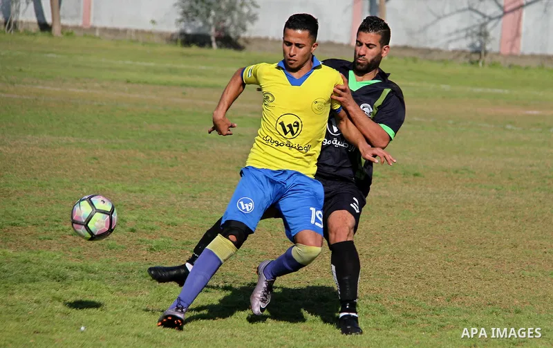 Palestinian Shabab Jabalia football club players (in yellow) and al-Hilal football club players (in black) compete during a football match at Beit Lahia Stadium in the northern Gaza Strip on March 11, 2018. Photo by Mahm...