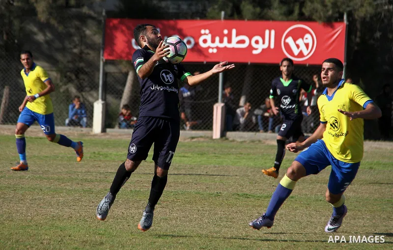 Palestinian Shabab Jabalia football club players (in yellow) and al-Hilal football club players (in black) compete during a football match at Beit Lahia Stadium in the northern Gaza Strip on March 11, 2018. Photo by Mahm...