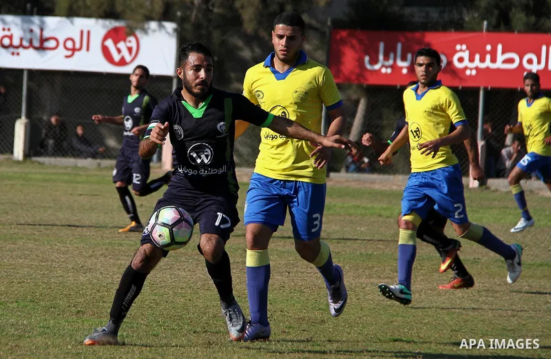 Palestinian Shabab Jabalia football club players (in yellow) and al-Hilal football club players (in black) compete during a football match at Beit Lahia Stadium in the northern Gaza Strip on March 11, 2018. Photo by Mahm...