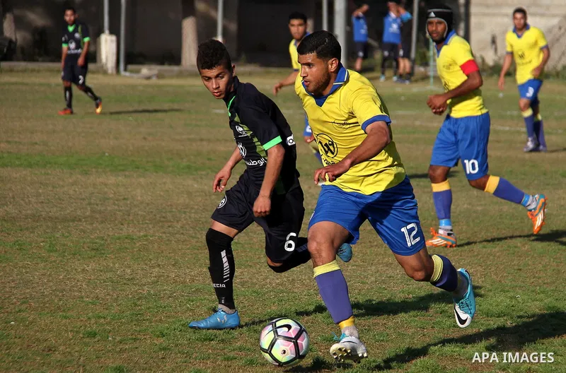 Palestinian Shabab Jabalia football club players (in yellow) and al-Hilal football club players (in black) compete during a football match at Beit Lahia Stadium in the northern Gaza Strip on March 11, 2018. Photo by Mahm...