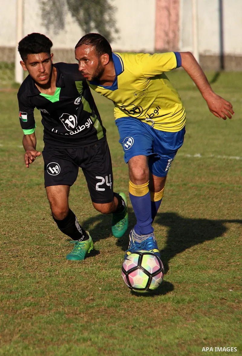 Palestinian Shabab Jabalia football club players (in yellow) and al-Hilal football club players (in black) compete during a football match at Beit Lahia Stadium in the northern Gaza Strip on March 11, 2018. Photo by Mahm...