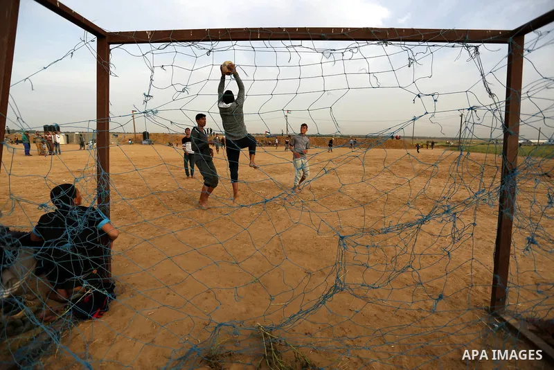 Palestinian youth play football during an event where activists set up tents near the Gaza-Israel border on the outskirts of the Khan Yunis in the southern Gaza Strip on March 28, 2018. Protesters plan to call for the ri...