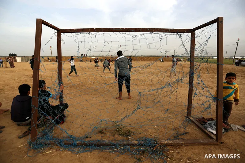 Palestinian youth play football during an event where activists set up tents near the Gaza-Israel border on the outskirts of the Khan Yunis in the southern Gaza Strip on March 28, 2018. Protesters plan to call for the ri...