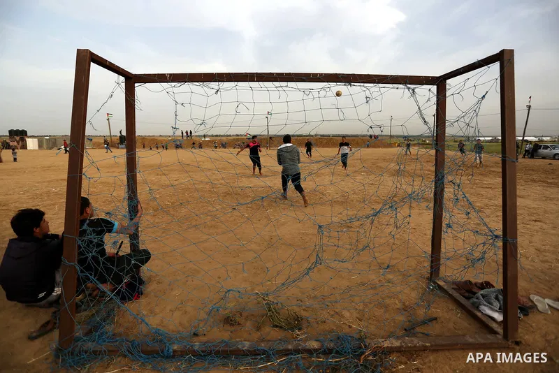 Palestinian youth play football during an event where activists set up tents near the Gaza-Israel border on the outskirts of the Khan Yunis in the southern Gaza Strip on March 28, 2018. Protesters plan to call for the ri...