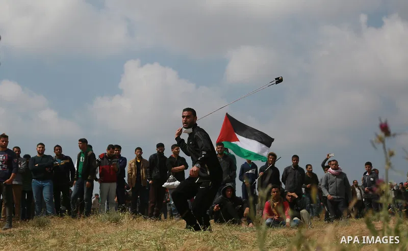 A Palestinian protester uses a slingshot to hurl stones toward Israeli security forces during clashes in a tent city protest along the Israel border with Gaza, demanding the right to return to their homeland, east of Gaz...