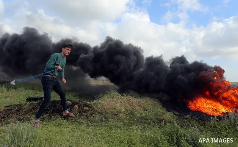 A Palestinian protester uses a slingshot to hurl stones towards Isareli security forces during clashes in a tent city protest at along the Israel border with Gaza, demanding the right to return to their homeland, in al-B...