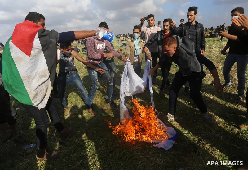Palestinian protesters burn an Israeli flag during clashes with Isareli security forces in a tent city protest at along the Israel border with Gaza, demanding the right to return to their homeland, in al-Bureij in the ce...