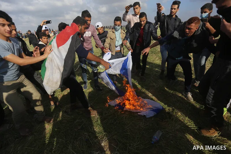 Palestinian protesters burn an Israeli flag during clashes with Isareli security forces in a tent city protest at along the Israel border with Gaza, demanding the right to return to their homeland, in al-Bureij in the ce...