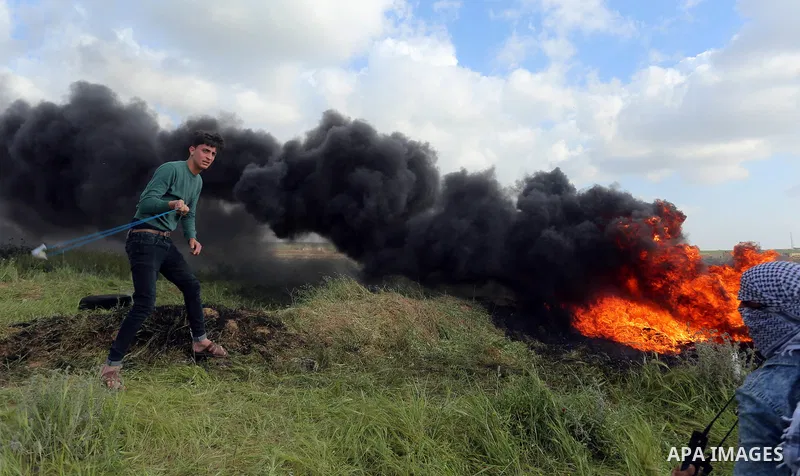 A Palestinian protester uses a slingshot to hurl stones towards Isareli security forces during clashes in a tent city protest at along the Israel border with Gaza, demanding the right to return to their homeland, in al-B...
