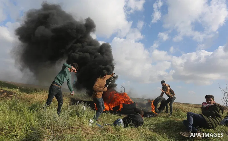 Palestinian protesters use slingshot to hurl stones towards Isareli security forces during clashes in a tent city protest at along the Israel border with Gaza, demanding the right to return to their homeland, in al-Burei...